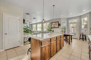 Kitchen featuring hanging light fixtures, a center island, light tile patterned flooring, brown cabinetry, and a kitchen breakfast bar