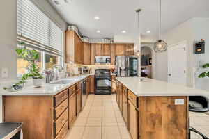 Kitchen featuring brown cabinetry, stainless steel appliances, decorative backsplash, light tile patterned floors, and arched walkways