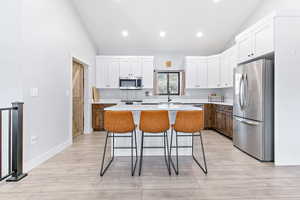 Kitchen with white cabinetry, stainless steel appliances, vaulted ceiling, light wood-type flooring, and recessed lighting