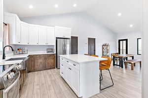 Kitchen with white cabinetry, appliances with stainless steel finishes, recessed lighting, a breakfast bar area, and light wood-style floors