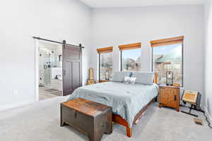 Bedroom featuring a barn door, a towering ceiling, light carpet, and ensuite bathroom