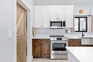 Kitchen featuring stainless steel appliances, white cabinetry, light wood finished floors, and light stone countertops