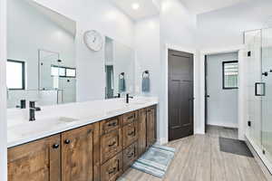 Full bath featuring double vanity, a baseboard heating unit, a shower stall, and wood finish floors