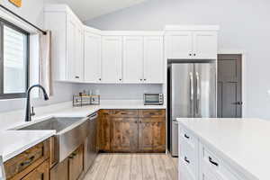 Kitchen with white cabinetry, appliances with stainless steel finishes, light wood-style flooring, light stone countertops, and vaulted ceiling