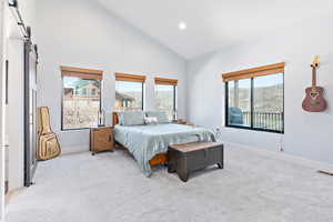 Bedroom with high vaulted ceiling, a barn door, light carpet, and recessed lighting