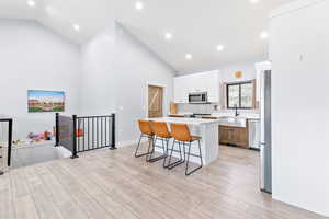 Kitchen featuring white cabinetry, a kitchen bar, a center island, light wood-style flooring, and recessed lighting