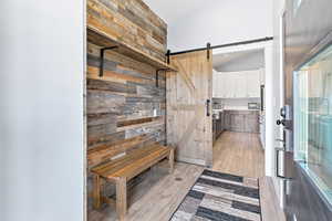 Mudroom featuring wood walls, vaulted ceiling, light wood-style flooring, and a barn door