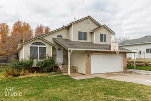 View of front of home with a shingled roof, driveway, a garage, a front lawn, and brick siding
