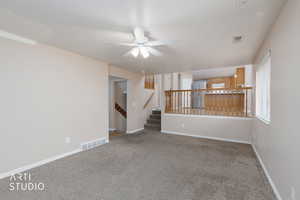 Carpeted spare room featuring ceiling fan and stairs