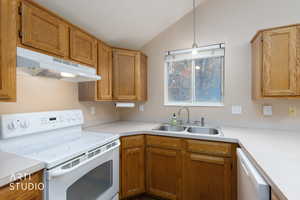 Kitchen with white appliances, pendant lighting, light countertops, under cabinet range hood, and lofted ceiling