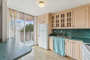 Kitchen featuring a wall of windows, white appliances, dark countertops, glass insert cabinets, and light wood-style flooring