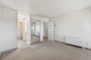 Unfurnished bedroom with a closet, light carpet, a textured ceiling, and connected bathroom