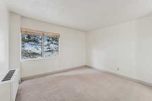 Empty room with light colored carpet, a textured ceiling, and a wall mounted AC