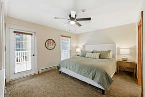 Bedroom with a baseboard heating unit, multiple windows, light carpet, and a ceiling fan