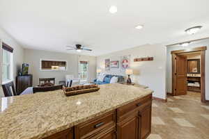 Kitchen with brown cabinets, light stone countertops, a ceiling fan, recessed lighting, and open floor plan
