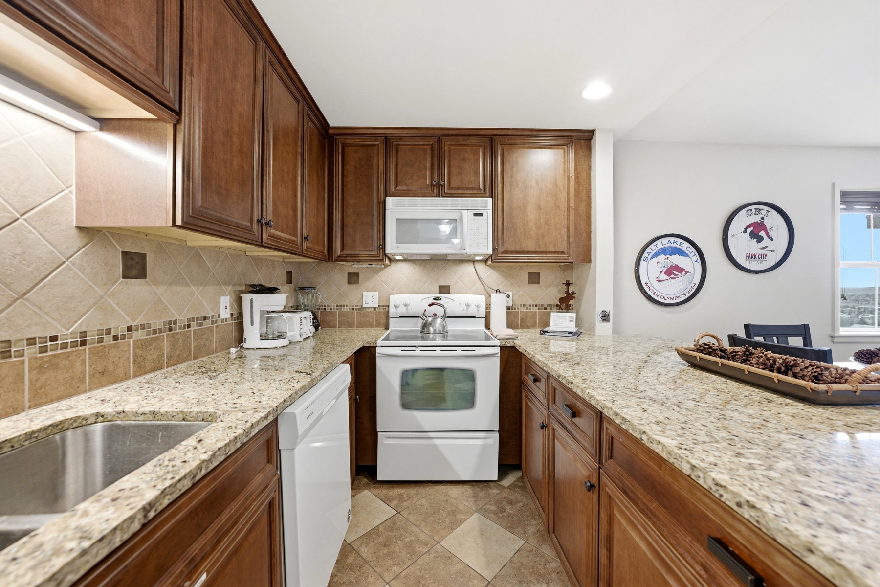 U-shaped kitchen featuring wood cabinetry, light-toned granite-style countertops, and a full tile backsplash with decorative accents