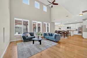 Living room with light wood-type flooring, ceiling fan, a chandelier, and a towering ceiling