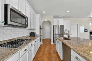 Kitchen with white cabinets, appliances with stainless steel finishes, light wood-style flooring, light stone countertops, and recessed lighting