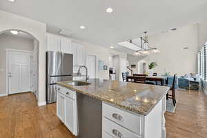 Kitchen with arched walkways, white cabinets, light stone counters, freestanding refrigerator, and recessed lighting