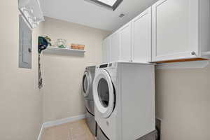 Washroom with light tile patterned floors, washer and dryer, cabinet space, and electric panel