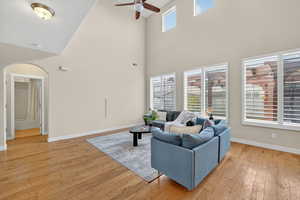 Living area with light wood-style flooring, ceiling fan, a towering ceiling, and arched walkways