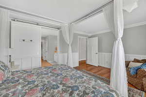 Bedroom with light wood-style floors, wainscoting, ornamental molding, and a decorative wall