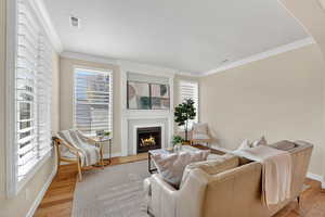 Living area featuring crown molding, a fireplace with flush hearth, and light wood finished floors