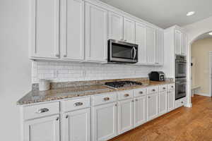 Kitchen with arched walkways, white cabinets, light stone countertops, light wood finished floors, and recessed lighting
