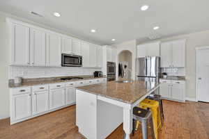 Kitchen featuring white cabinets, backsplash, light stone counters, a breakfast bar area, and recessed lighting
