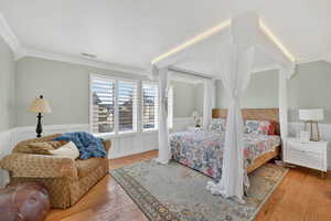 Bedroom featuring a wainscoted wall, light wood-type flooring, crown molding, and a decorative wall