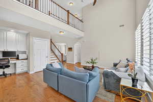 Living room with built in study area, arched walkways, light wood-style floors, stairway, and a high ceiling