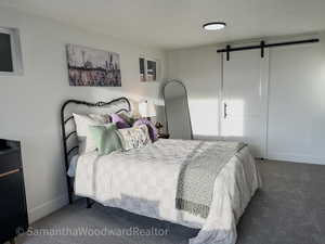 Bedroom featuring a barn door, carpet floors, and a textured ceiling