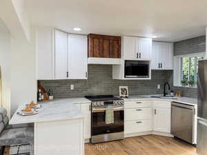 Kitchen featuring white cabinets, appliances with stainless steel finishes, light stone counters, light wood-style flooring, and a peninsula