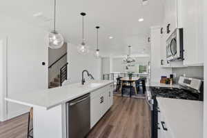 Kitchen featuring an expansive island with a stainless steel dishwasher, white cabinetry with black hardware, and pendant lighting
