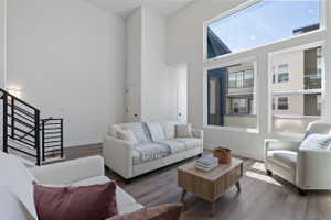 Living area featuring high ceilings, wood-finish flooring, a contemporary staircase with black railings, and multiple large windows