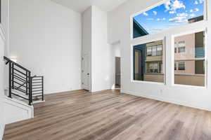Unfurnished living room with a towering ceiling, light wood-style flooring, and stairway