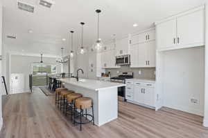 Kitchen featuring light wood-finish flooring, white cabinetry with matte black hardware, a light-toned backsplash, a gas range with a stainless steel microwave, and pendant lighting