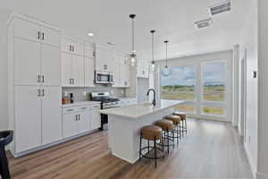 Modern kitchen featuring white cabinetry, a large center island with seating, pendant lighting, stainless steel appliances, and wood-finish flooring