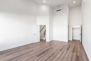 Unfurnished bedroom featuring a towering ceiling, light wood-style floors, a spacious closet, a wall mounted AC, and recessed lighting