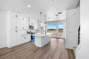 Kitchen featuring stainless steel appliances, a center island with sink, pendant lighting, white cabinets, and dark wood finished floors