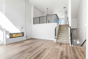 Unfurnished living room featuring high vaulted ceiling, a glass covered fireplace, a chandelier, light wood finished floors, and stairs