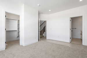 Unfurnished bedroom with a walk in closet, light colored carpet, recessed lighting, and ensuite bath