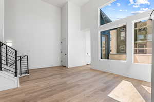 Spare room featuring a towering ceiling, stairway, and light wood-style floors