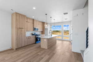 Kitchen featuring modern cabinets, appliances with stainless steel finishes, a center island with sink, light wood-style floors, and pendant lighting