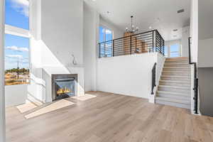 Unfurnished living room with healthy amount of natural light, a glass covered fireplace, light wood-style floors, a high ceiling, and stairway