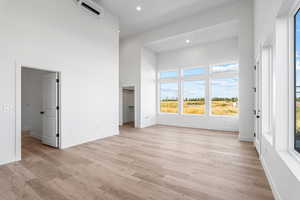 Unfurnished living room with a high ceiling, light wood finished floors, a wall unit AC, and recessed lighting