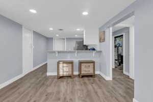 Kitchen featuring a breakfast bar, white cabinets, light wood finished floors, light stone counters, and recessed lighting