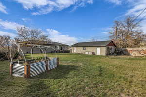 View of grassy yard featuring a garden and an outbuilding