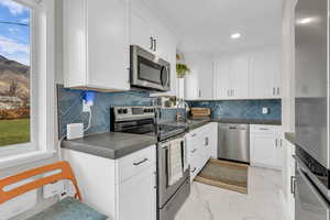 Kitchen featuring stainless steel appliances, light marble finish floors, white cabinets, tasteful backsplash, and recessed lighting