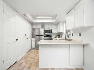 Kitchen featuring a tray ceiling, light countertops, white cabinetry, a peninsula, and stainless steel appliances